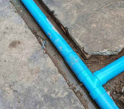 blue PVC pipe laid in a trench showing joint connections and surrounding concrete surface for plumbing installation two pipes in place