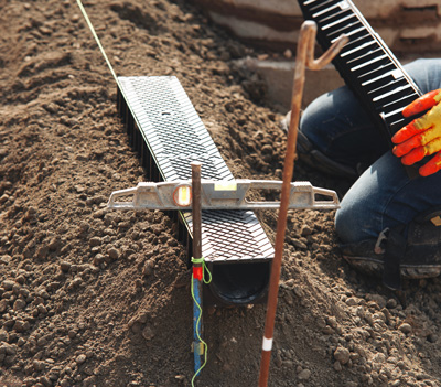person using a level tool aligned with drainage trench in dirt landscape