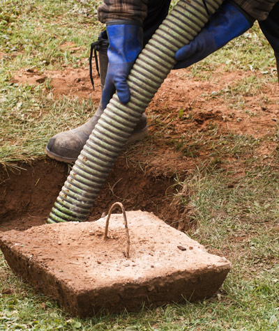 person using a hose to pour concrete into a hole for foundation work landscaping project