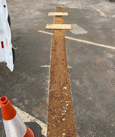 excavation trench in parking lot with wooden planks and traffic cone showing construction area