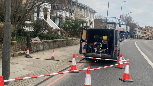 work van parked on the street with construction equipment and safety cones nearby blocking off area for maintenance task